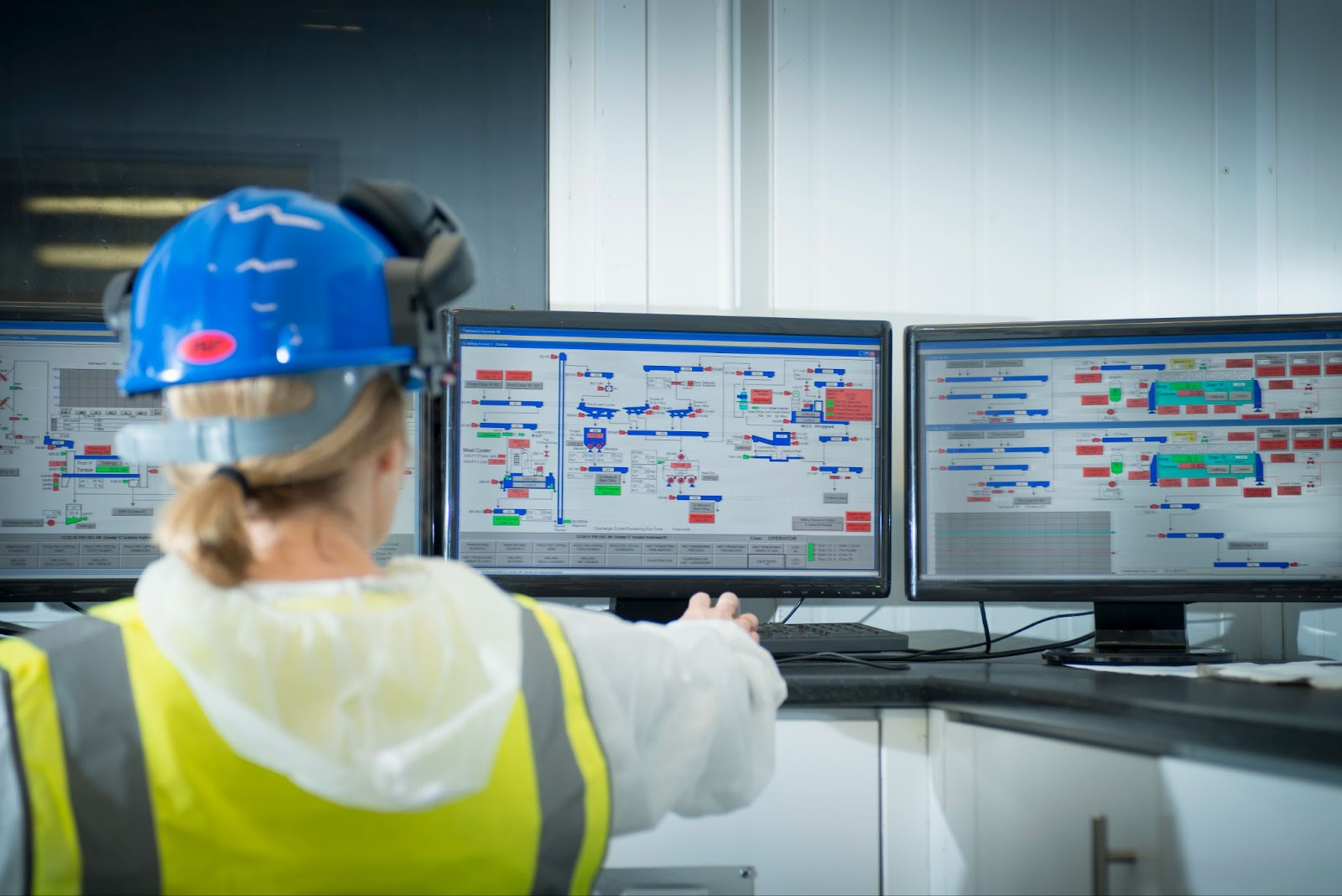 An industrial operator monitoring multiple screens displaying real-time data from a process control system.
